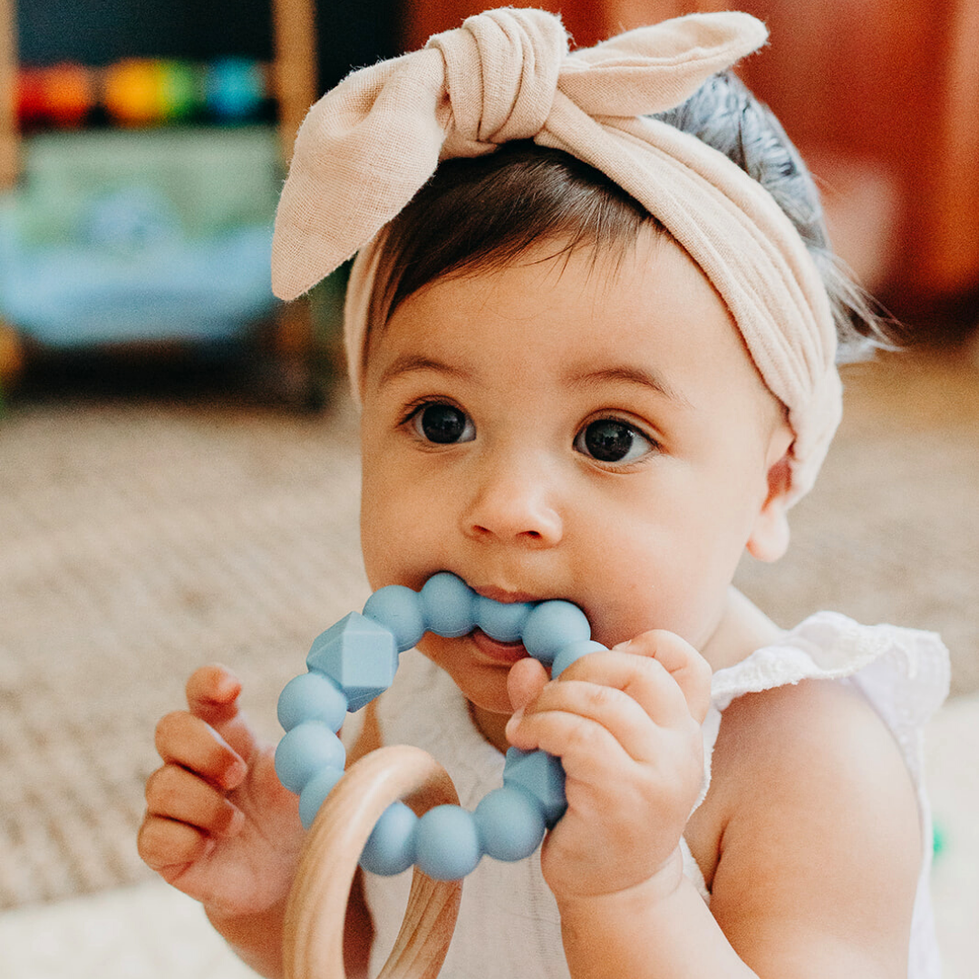 Baby girl chewing silicone and wood teether